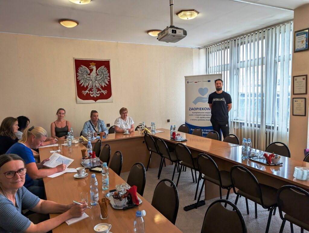 uczestnicy spotkania siedzą przy stole , słuchają wykładu prowadzącego.