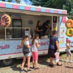 Dzieci stojące przy food trucku z donutami i lodami.
